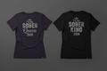 Two t-shirts, one purple and one black, with 'I'm his Sober Queen 2026' and 'I'm her Sober King 2026' text on a dark background.